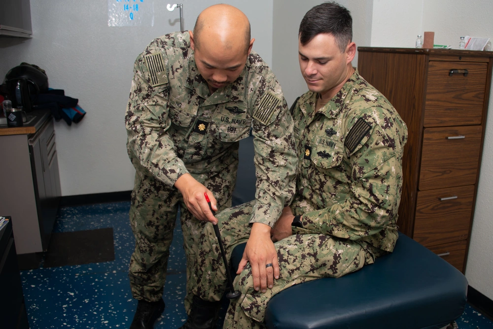 Navy doctor examining a sailor's knee in a medical setting, potentially related to USS Carl Vinson medical operations.