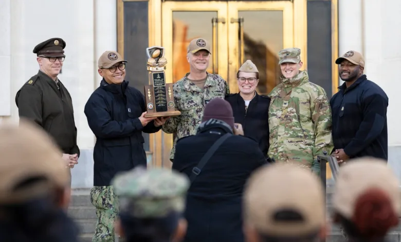 Navy personnel holding the Army Navy Blood Drive trophy, smiling for a photo.