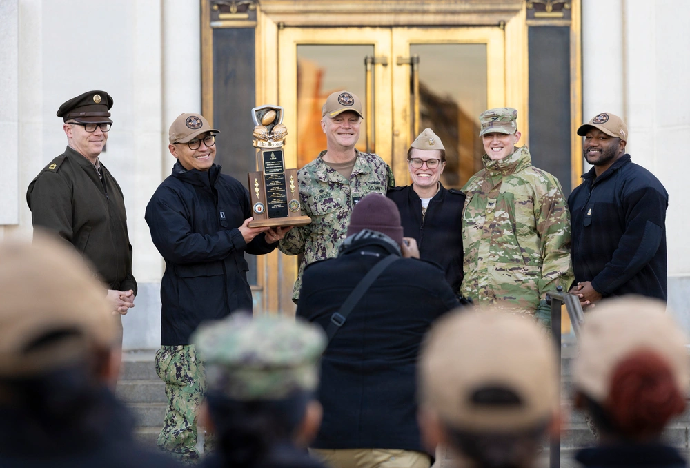 Navy personnel holding the Army Navy Blood Drive trophy, smiling for a photo.