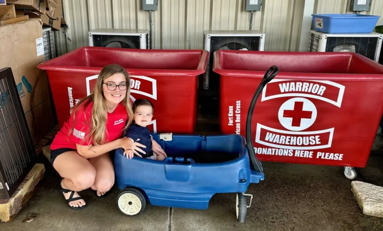 Volunteer with child by Red Cross bins at Fort Knox. "Warrior Warehouse Donations Here Please" text visible.
