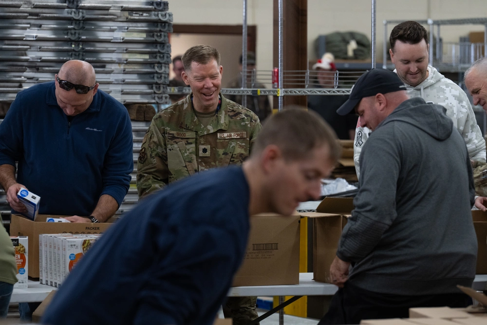 Volunteers, including an Air Force officer, assemble holiday baskets with food items for families.