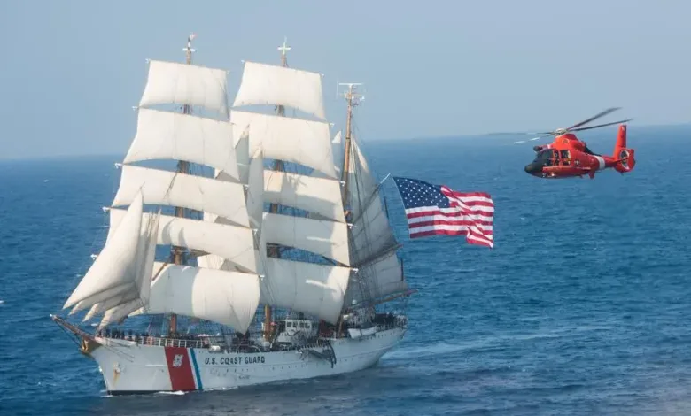 Coast Guard's Eagle sailing ship with American flag, accompanied by a red Coast Guard helicopter.