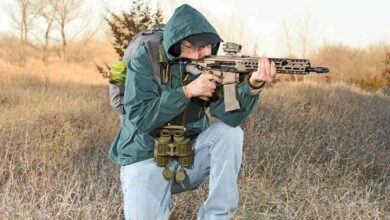 Man kneeling, aiming SIG SAUER MCX-SPEAR LT rifle in field.