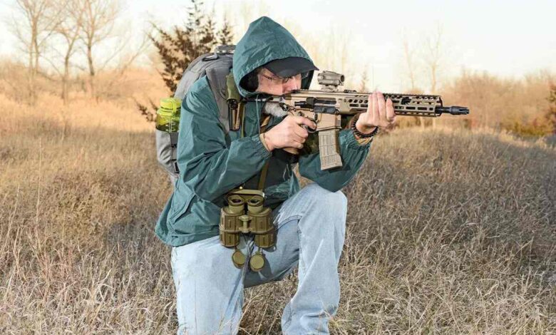 Man kneeling, aiming SIG SAUER MCX-SPEAR LT rifle in field.