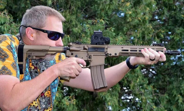 Man shooting an AR-15 pistol with a tan finish and red dot sight.