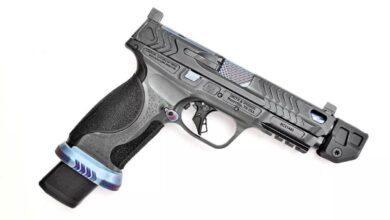 Custom Smith & Wesson M&P V series pistol with intricate slide design and extended magazine. Text: "CAUTION-CAPABLE OF FIRING WITH MAGAZINE REMOVED