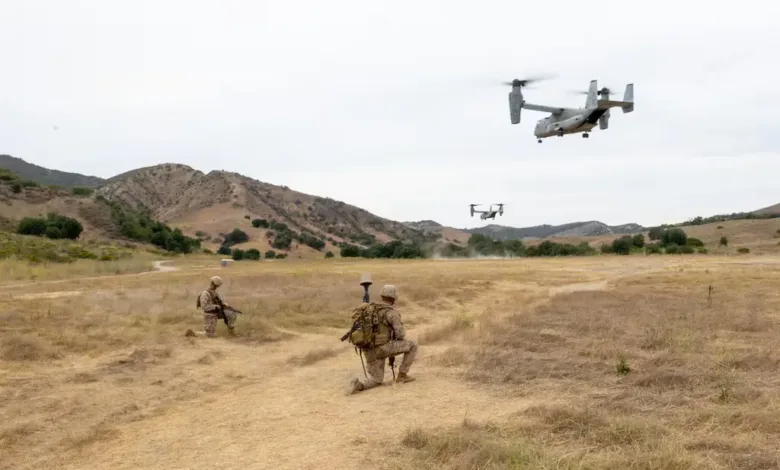 Marines kneeling as V-22 Osprey aircraft land during GPS landing system training.