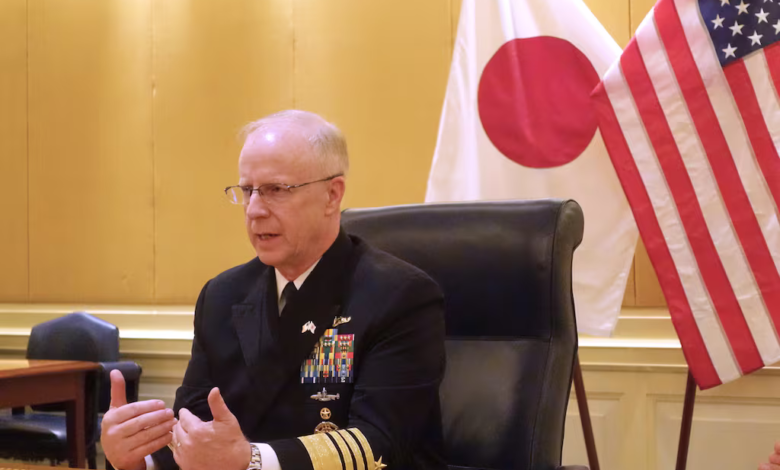 US admiral speaking with flags of Japan and the US behind him.