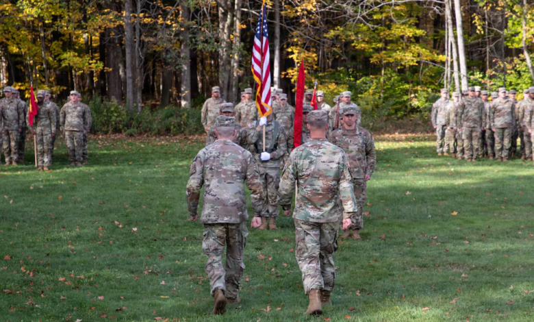 US Army soldiers in formation during an outdoor ceremony, flags visible.