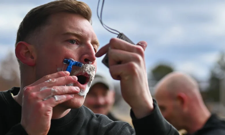 Soldier shaves mustache with razor and shaving cream outdoors.