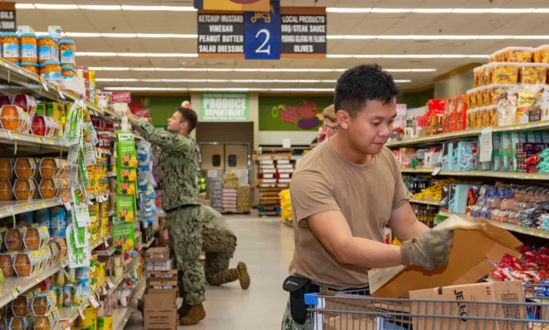 Troops restocking shelves at a commissary. "Produce Department" sign is visible. As federal food assistance runs out.