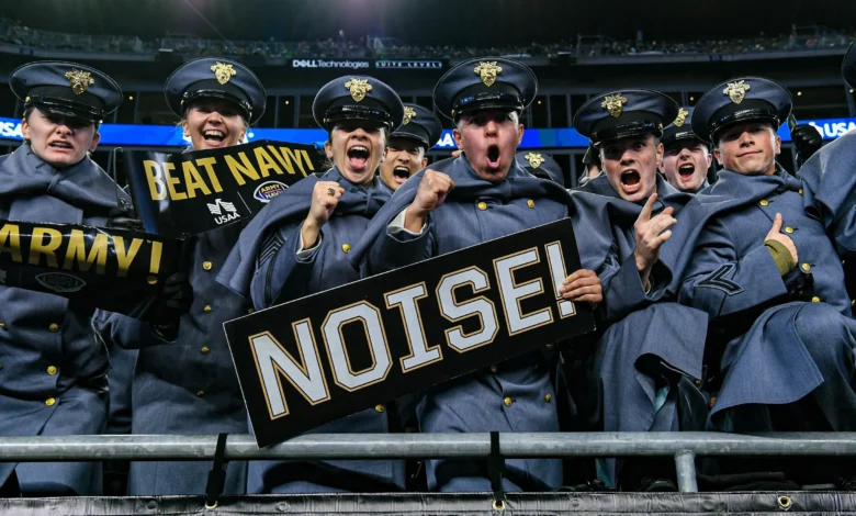 Enthusiastic Army cadets in uniform cheer at the Army-Navy game, holding signs: "Beat Navy!" and "Noise!