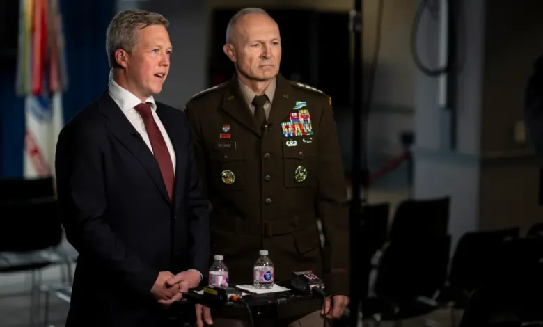 Man in suit and Army officer in uniform at a press conference.