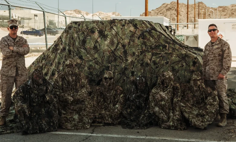 Marines hidden in camouflage, two standing guard. Six Marines total.