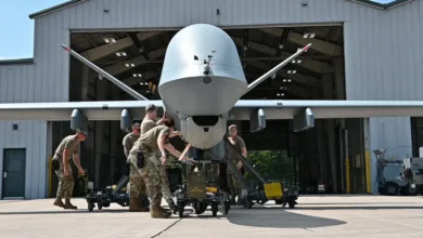 Air Force personnel move a large drone on a wheeled platform inside a hangar.