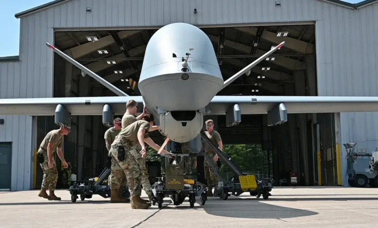 Air Force personnel move a large drone on a wheeled platform inside a hangar.
