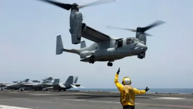 V-22 Osprey tiltrotor aircraft landing on a U.S. Navy aircraft carrier flight deck, with flight deck crew.