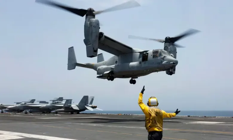 V-22 Osprey tiltrotor aircraft landing on a U.S. Navy aircraft carrier flight deck, with flight deck crew.