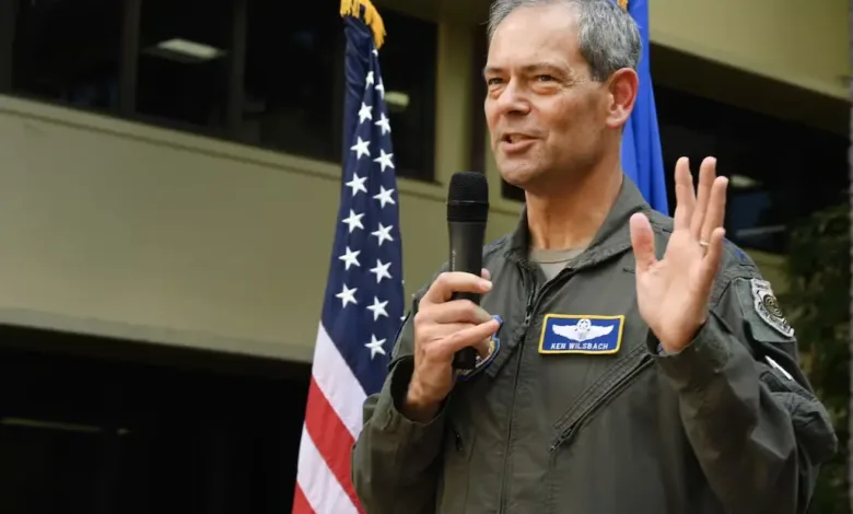 General Ken Wilsbach speaking in front of US flag. Name tag reads "Ken Wilsbach.