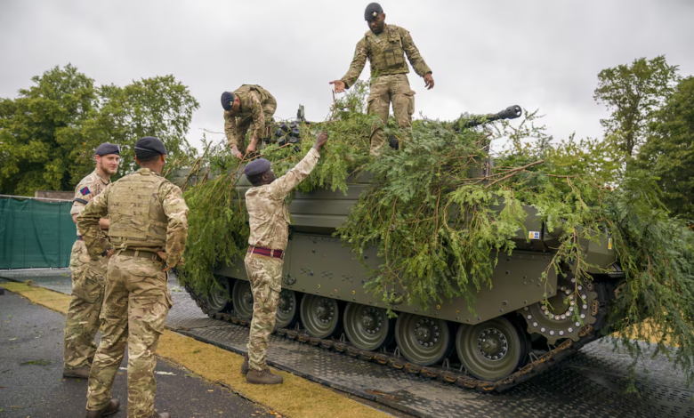 British Army soldiers camouflage an Ajax vehicle with foliage.