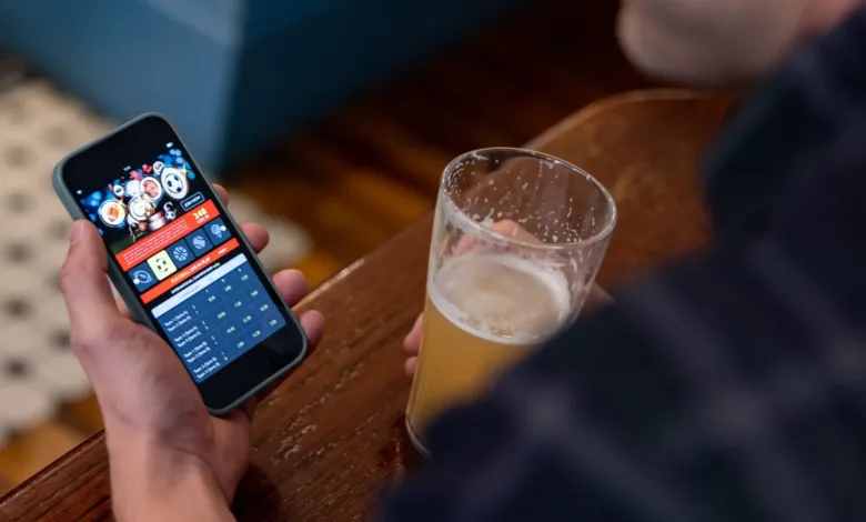Man using gambling app on phone while holding beer. "Join Now. Football Live in Play.