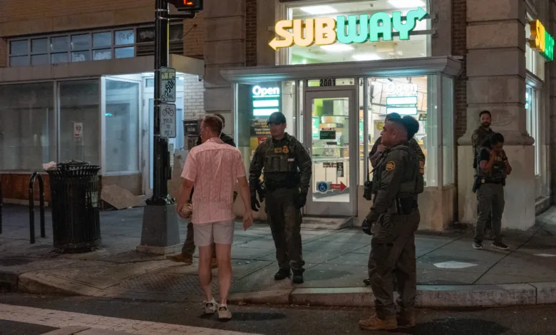 Subway storefront at night with law enforcement officers standing outside. Text: "Subway," "Open," "Yield.