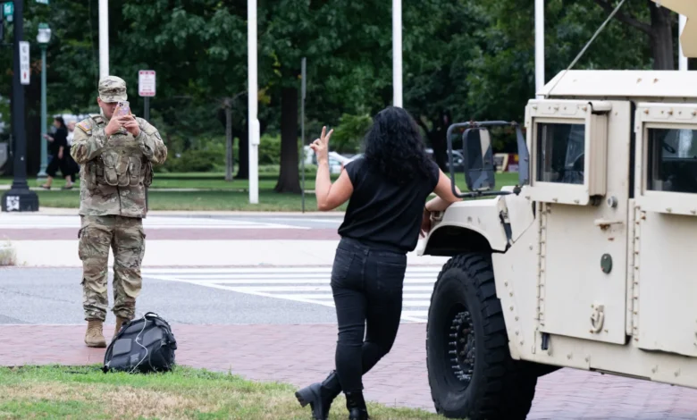 Guard soldier takes photo of woman posing by military vehicle in DC. "Guard troops in DC" SEO keyword used.