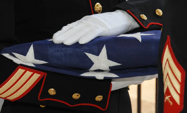 Folded American flag held by a Marine in dress uniform.