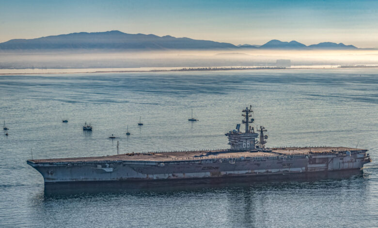 USS Nimitz aircraft carrier sailing near Bremerton, with mountains in the background.