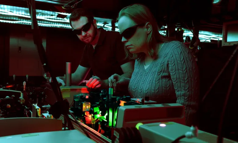 Researchers in lab with advanced tech and lasers, wearing protective eyewear.