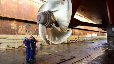 Massive ship propeller being inspected by US Navy personnel in dry dock.