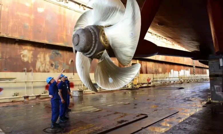 Massive ship propeller being inspected by US Navy personnel in dry dock.