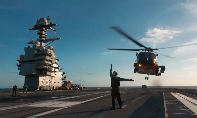 Helicopter landing on the USS Gerald R. Ford aircraft carrier deck, with flight deck crew guiding.