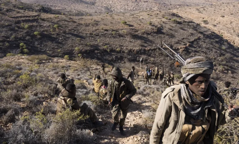 Group of armed fighters in a dry, mountainous landscape.