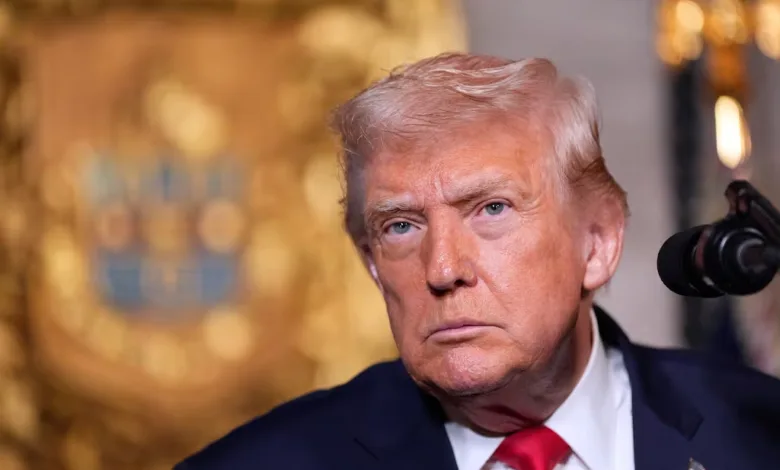 Donald Trump looking serious in a suit and red tie.