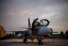 Swedish air force personnel servicing a Gripen fighter jet on the tarmac at dusk.