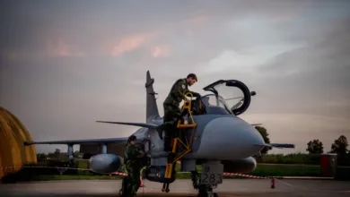 Swedish air force personnel servicing a Gripen fighter jet on the tarmac at dusk.