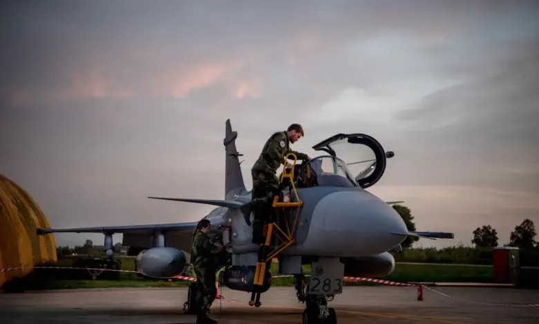 Swedish air force personnel servicing a Gripen fighter jet on the tarmac at dusk.