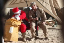 Santa with a Marine in a desert camp, sharing holiday cheer.
