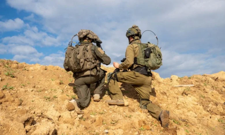 Two soldiers kneeling on a sandy hill wearing tactical gear and backpacks.
