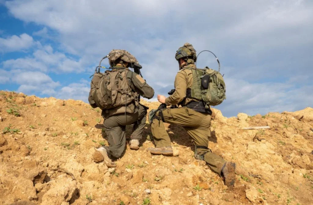 Two soldiers kneeling on a sandy hill wearing tactical gear and backpacks.