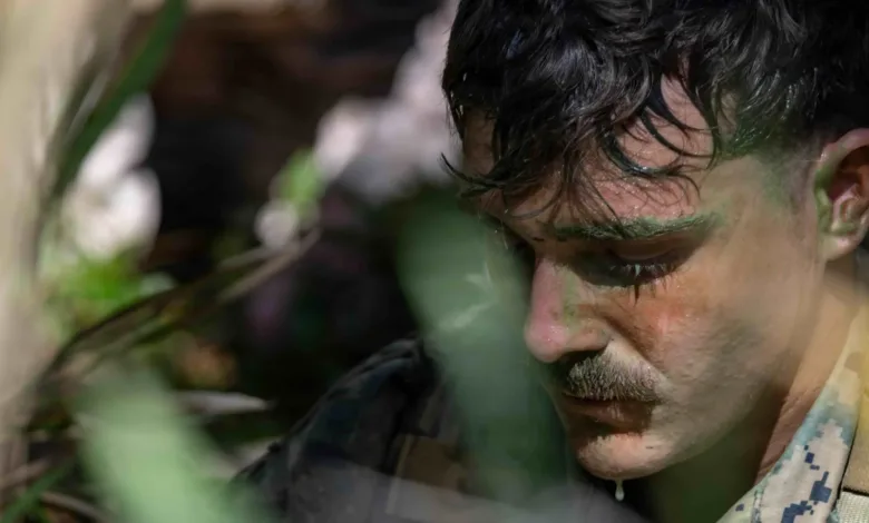 Close-up of a soldier with a mustache, face covered in sweat, possibly facing pay issues.