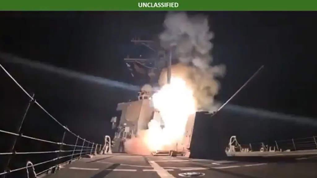 US Navy missile launch from warship at night, with bright flash and smoke. "UNCLASSIFIED" text visible.