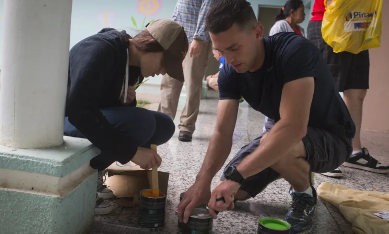 Volunteers painting a building, preparing cans of paint.