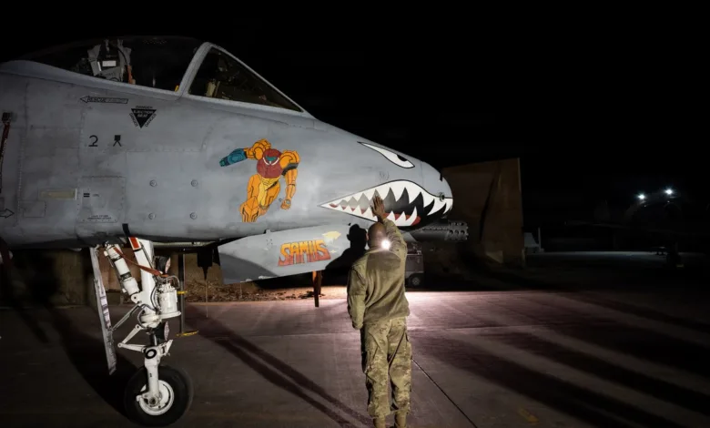 A-10 Warthog with 'Metroid' nose art being inspected at night on the flight line.
