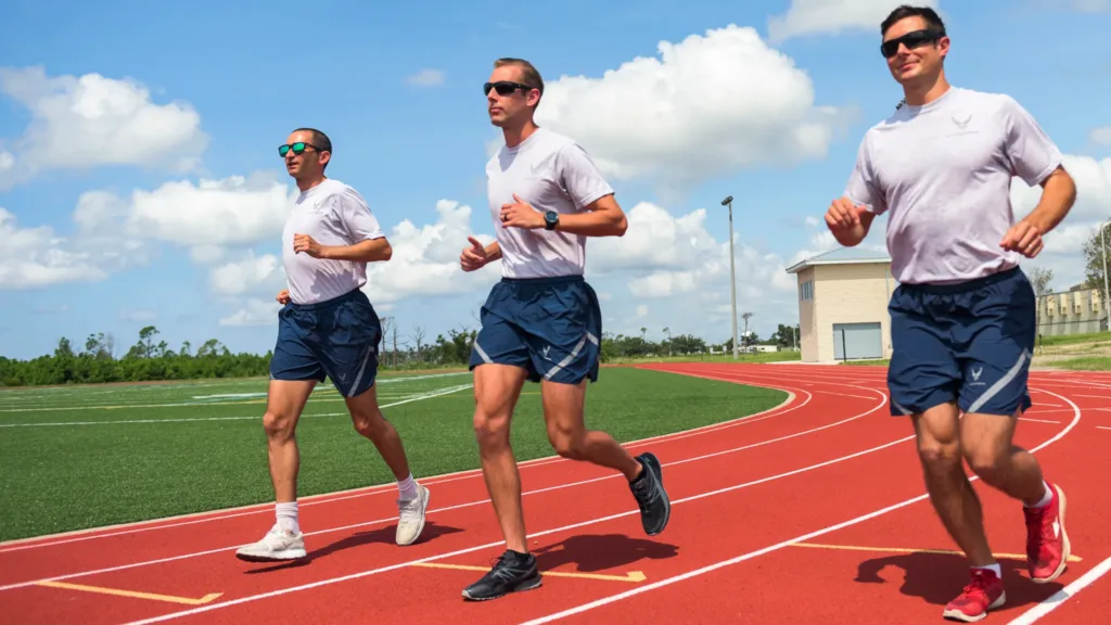 Three Air Force members running on a track in athletic gear.