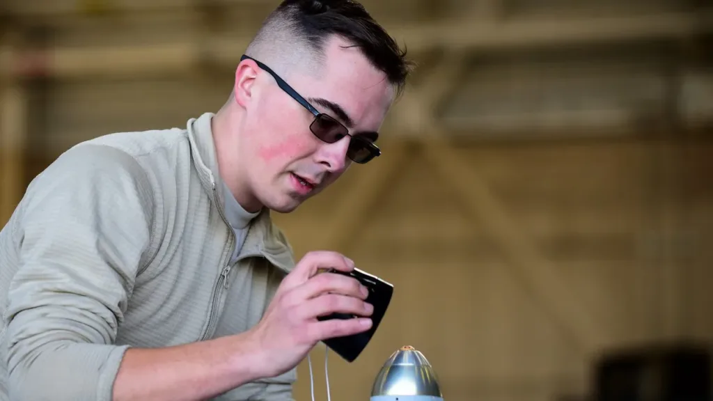 Airman inspecting missile component with smartphone in hangar. Military technician, aircraft maintenance.