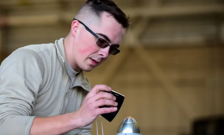 Airman inspecting missile component with smartphone in hangar. Military technician, aircraft maintenance.