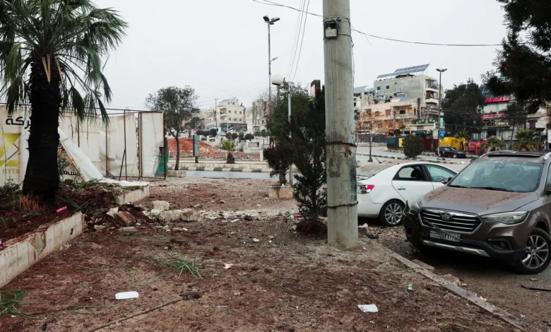 Street scene with damaged landscape, cars, and buildings under a cloudy sky.