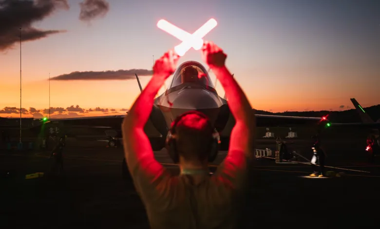 F-35 fighter jet guided by ground crew at sunset with signal wands.